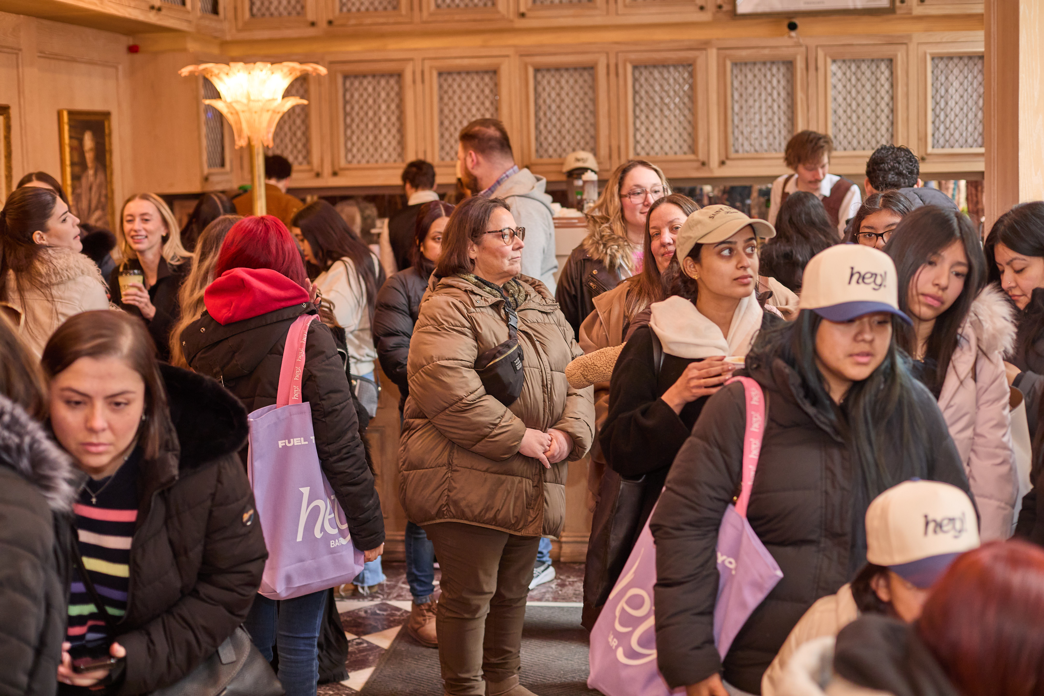A group of people inside a coffee shop wearing hey hats and hey totes.