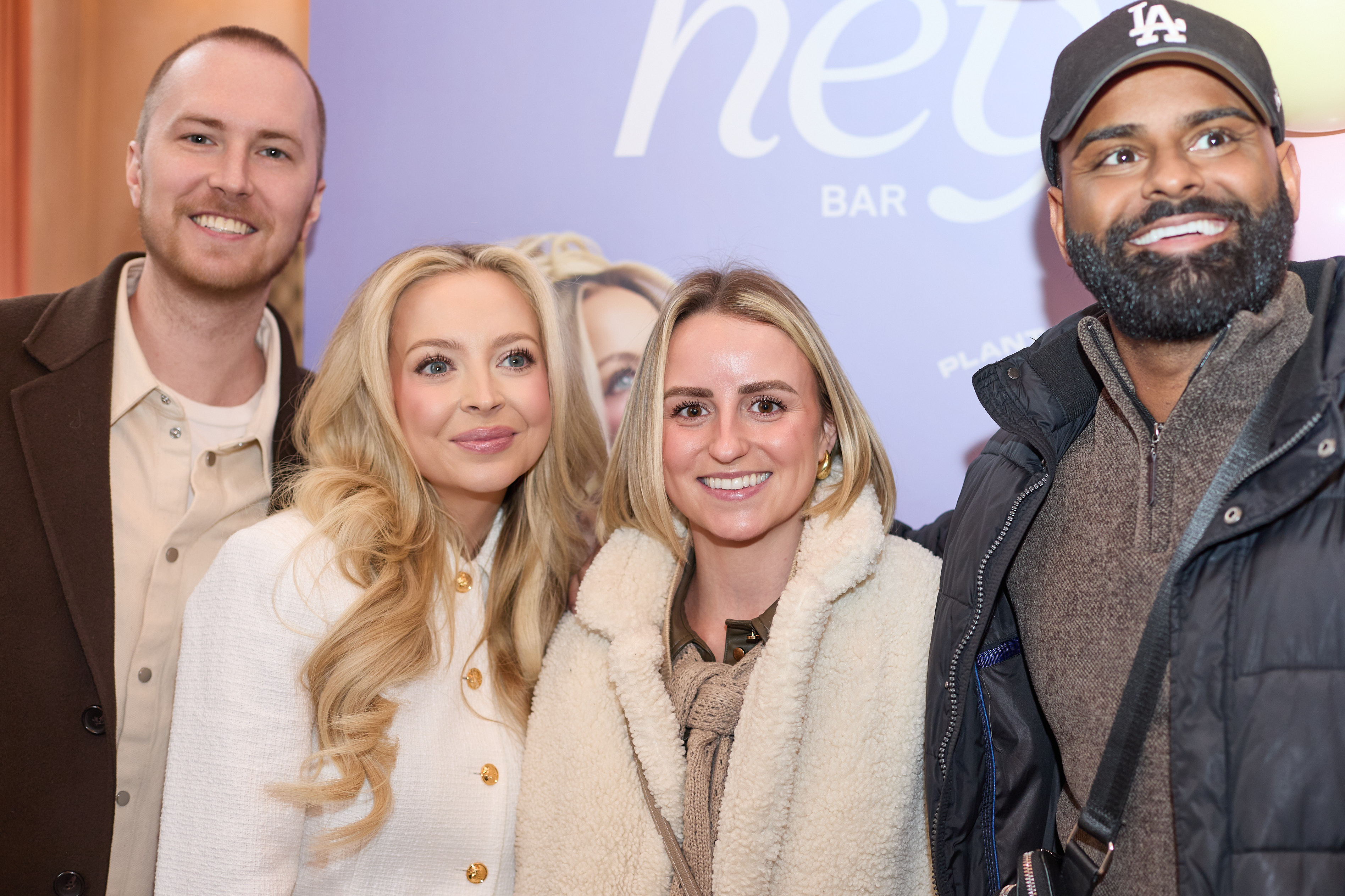 Kay and Tay Dudley posing together with two people in front of a colorful background with 'hey' visible.