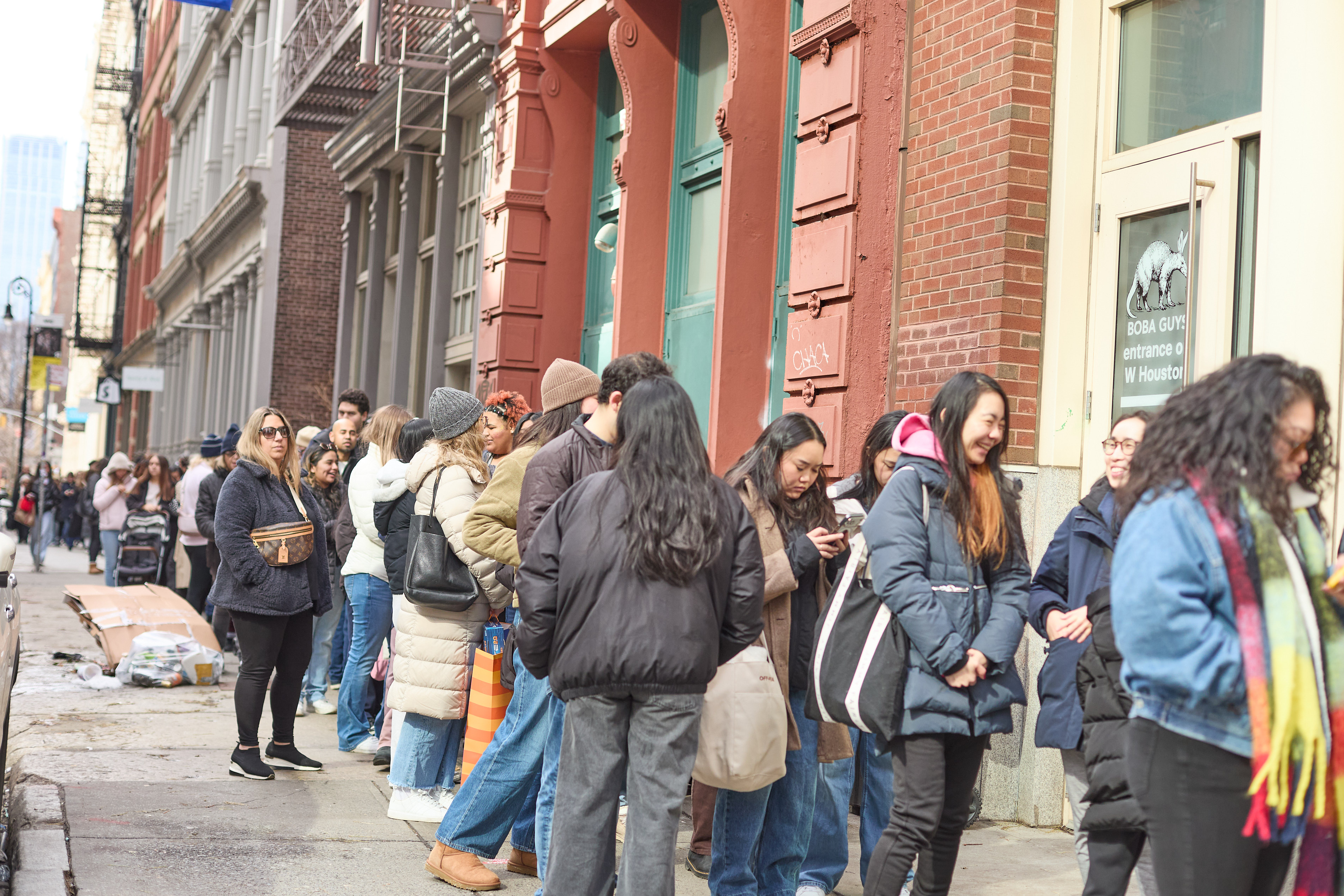 People waiting in line on a city street with brick buildings.