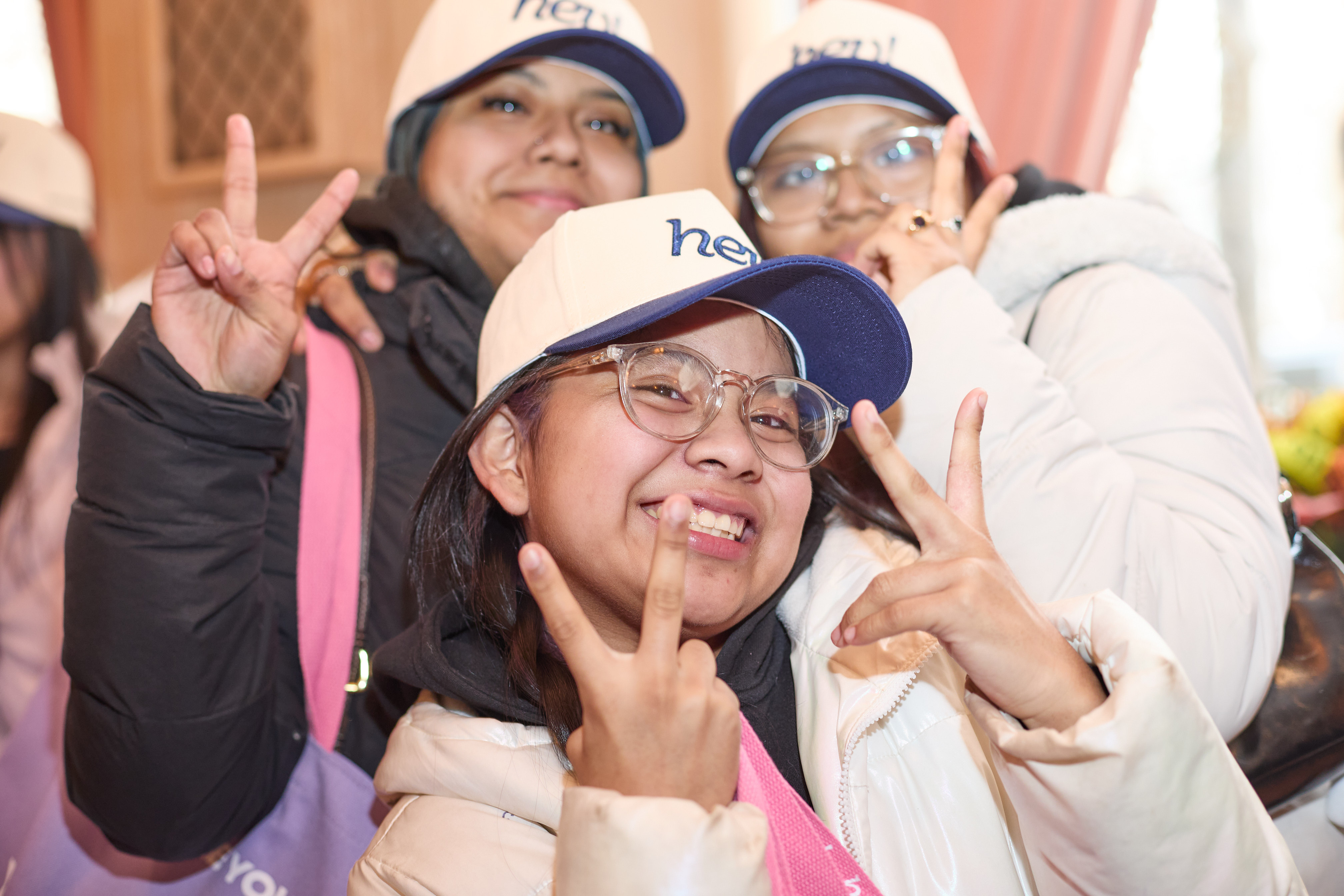 Three people wearing hats with 'hey' branding, making peace signs.