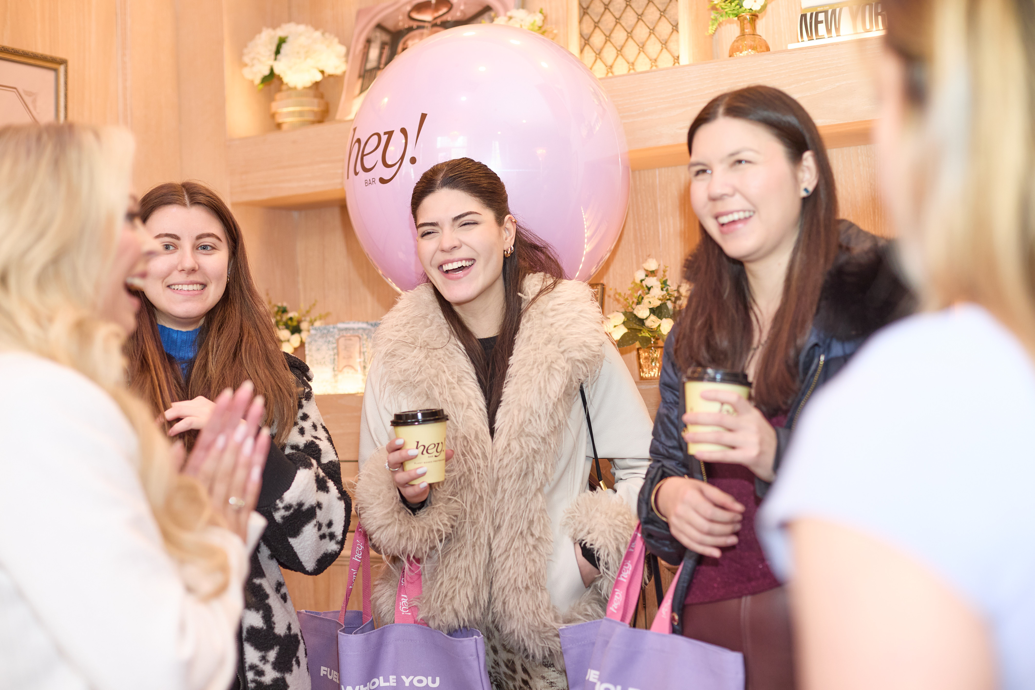 Group of women celebrating with balloons and coffee in a cozy indoor setting
